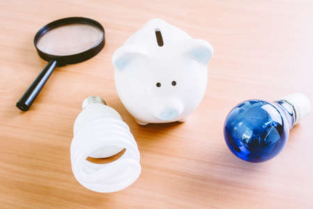 Energy saving lamp with piggy bank on wooden tableの写真素材