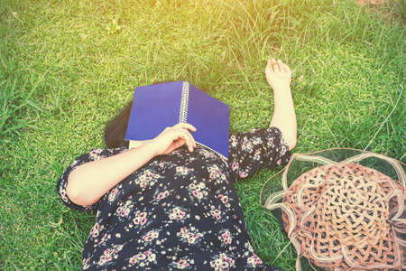 Woman lying down on grass with bookの写真素材