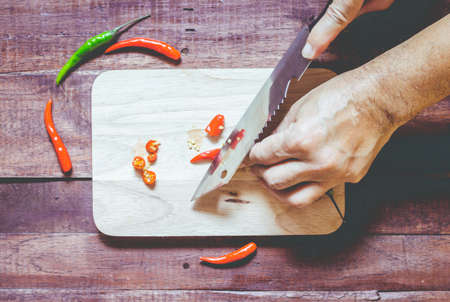 Hand slicing chili pepper with Knife on chopping board on wooden backgroundの写真素材