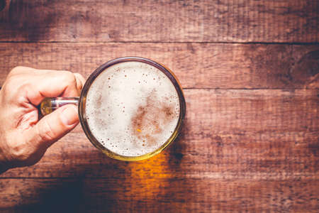 Hand holding a glass of beer on wooden tableの写真素材