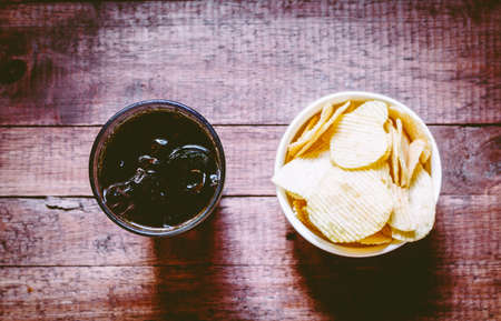 Cola in glass and potato chips on wooden background