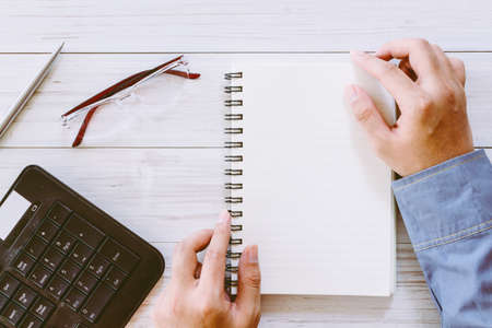 Hands holding book on a wooden table with office supplies