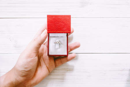 Hand holding engagement diamond ring on wooden tableの写真素材