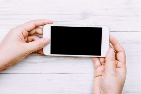 Women hand holding smartphone on wooden backgroundの写真素材