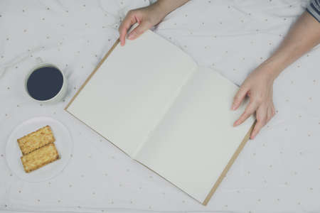 Woman reading book and drinking coffee in bed in the morning