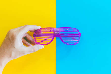 Hand holding disco party glasses on colourful background