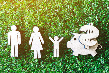 Wooden family and piggy bank on green grass backgroundの写真素材