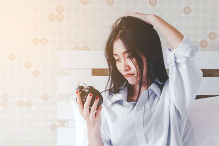 Woman holding alarm clock in bedroom at homeの写真素材