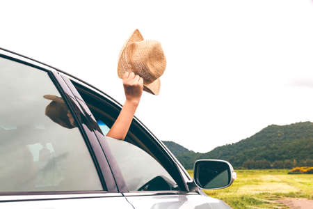 Woman hand holding hat on the car relaxing and happy traveler with mountain backgroundの写真素材