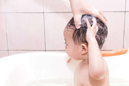 Mother washing baby head with shampoo in bathの写真素材