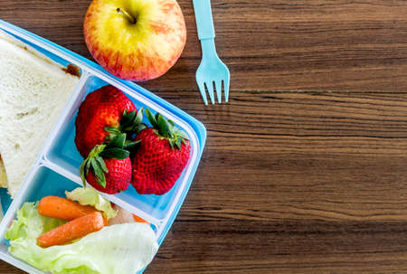 Lunch box with vegetables and slice of bread for a healthy school lunch on wooden tableの写真素材