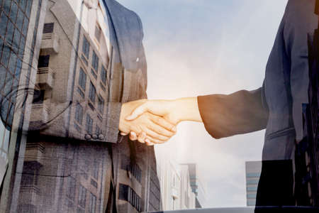 Handshake of business partners on office building background - Double exposure photoの写真素材