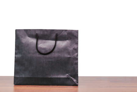 Black paper shopping bag on wooden table isolated on whiteの写真素材