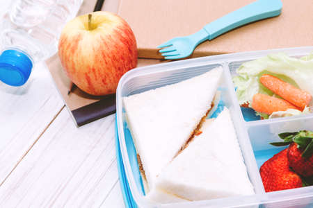 Lunch box with vegetables and slice of bread for a healthy school lunch on wooden tableの写真素材