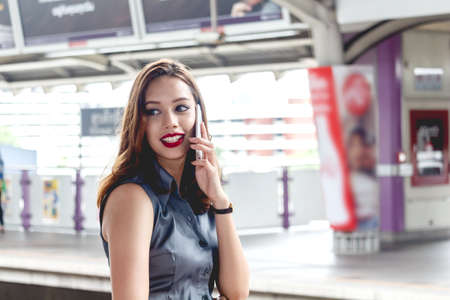 Young woman holding smartphone and standing at train station  の写真素材