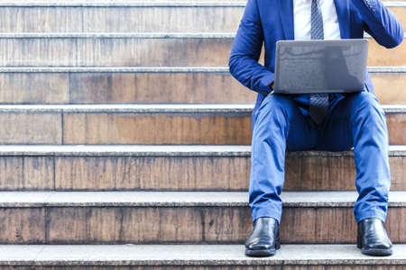 Businessman sitting on stairs and using laptopの写真素材