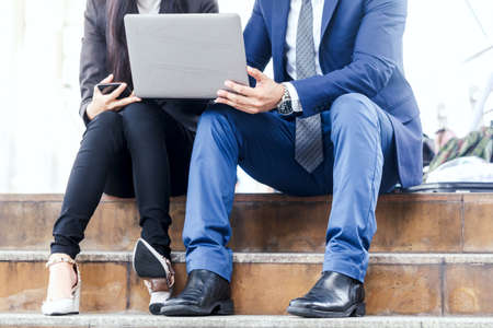 Business woman and businessman sitting on stairs and using laptopの写真素材