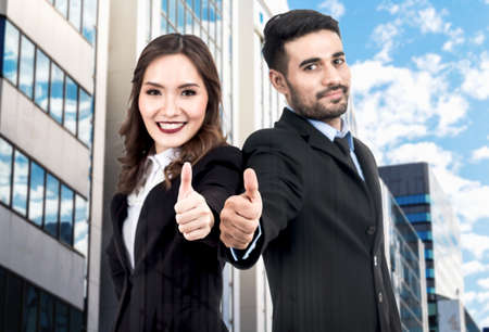 Businessman and business woman show thumb up on office buildings background の写真素材