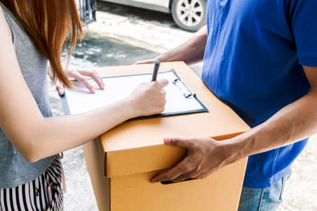 Woman putting signature in clipboard on cardboard box with delivery man