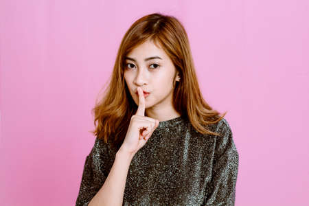 Woman quiet gesture with finger on pink backgroundの写真素材