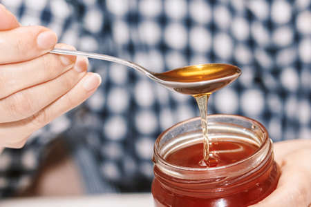 Woman hand holding glass jar of honeyの写真素材
