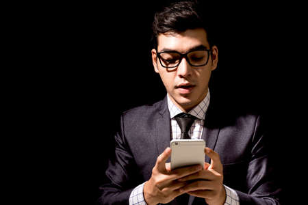 Businessman in elegant black suit using smartphone on black backgroundの写真素材
