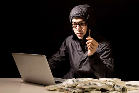 Hacker in a hood stealing information with computer on dark background