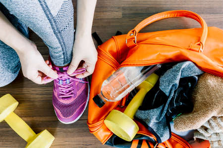 Woman tying shoelaces with bag and fitness equipmentの写真素材