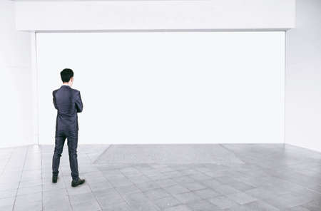 Businessman in black suit standing in empty interior with mock up white spaceの写真素材