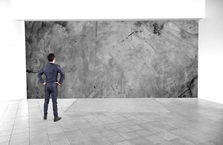 Businessman in black suit standing at empty interior with stone texture space