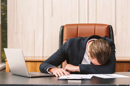 Tired businessman sleeping with laptop on the table at officeの写真素材
