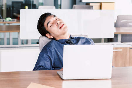 Tired businessman sleeping with laptop on the table at officeの写真素材
