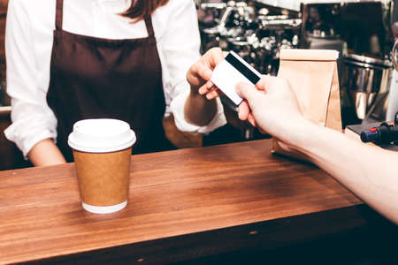 Female barista  taking a credit card from customer in coffee shopの写真素材