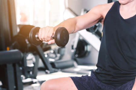 Fitness man doing weights exercises with dumbbell sitting at the gymの写真素材