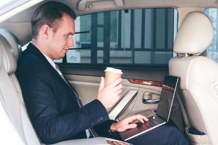 Handsome businessman working on laptop computer sitting on back seat of a carの写真素材