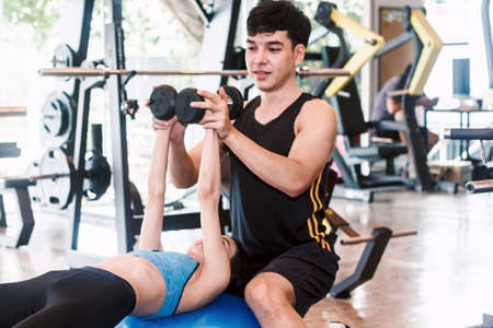 Handsome trainer and fitness woman with weight training equipment at  the gym.fitness and lifestyle...