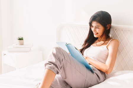 Woman reading book on bed in the morningの写真素材