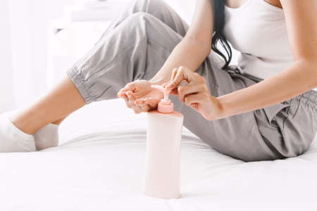 Woman applying cream on hand on bed