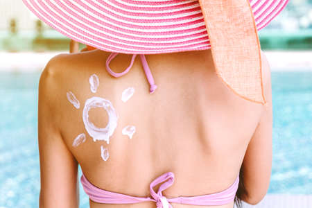 Woman applying suncream with sun drawn on back at resort spa pool
