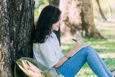Woman with pen writing on a notebook sitting on grass in parkの写真素材