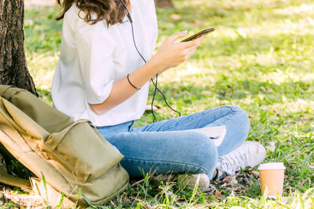 Woman relax and use smartphone sitting on grass in parkの写真素材