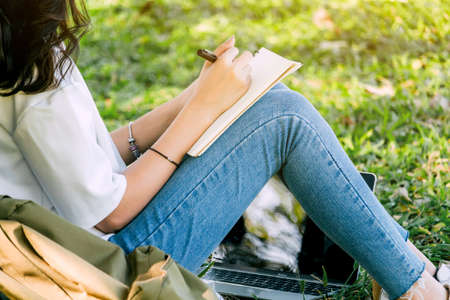 Woman with pen writing on a notebook sitting on grass in parkの写真素材