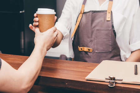 Woman barista giving coffee cup to customer at cafeの写真素材