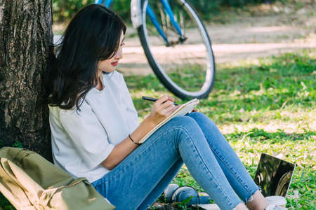 Woman with pen writing on a notebook sitting on grass in parkの写真素材