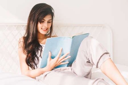 Woman reading book on bed in the morning