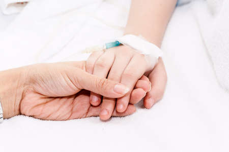 Mother holding little girl hand with IV saline intravenous in hospital