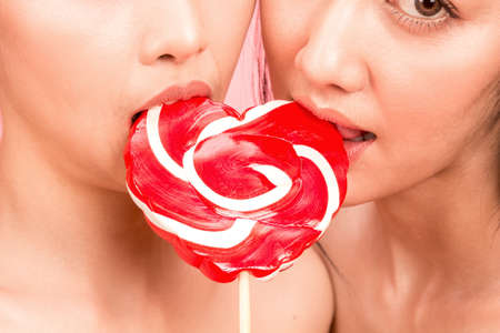 Portrait of two sexy women holding and lick big pink lollypop