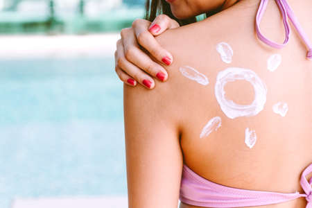 Woman wearing two piece bikini applying suncream with sun drawn on back at resort spa poolの写真素材