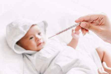 Mother holding thermometer of her ill baby.Sick baby on bed with fever measuring temperatureの写真素材
