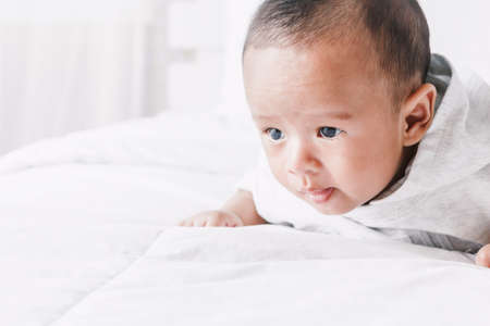 Portrait of baby relaxing on white bed in roomの写真素材